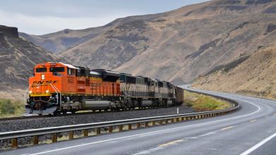A photograph of a train. There is a road next to the train, and there are two hills behind the train.