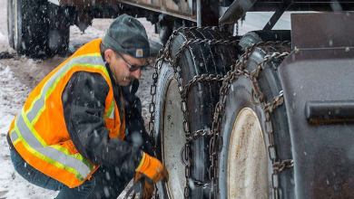 Driver putting chains on his tires as snow falls.