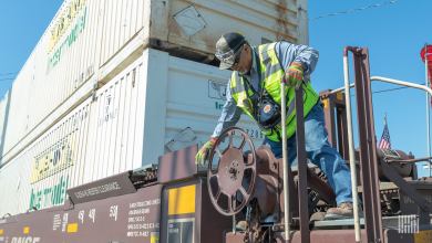 A photograph of a man turning the steel wheel of an intermodal car.