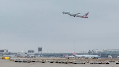 A plane rises above airport with cargo equipment in foreground.