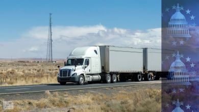 Tractor-trailer on a highway with communications towers in the background.