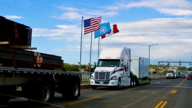 A tractor-trailer passes by a US, Canadian and United Nations flagl