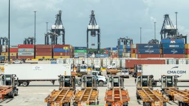 A view of cranes, trailers, containers and trucks at a port on a sunny day.