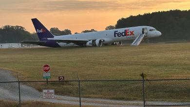Sunrise over the trees with a damaged FedEx jet sitting in the grass at an airport.