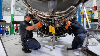 Two men on their knees working to overhaul a large aircraft engine.