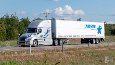 A silver sleeper cab pulling a Landstar dry van trailer on a highway