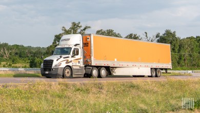 A white Schneider daycab pulling an orange Schneider dry van trailer
