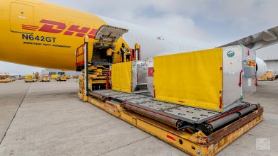 A mustard-yellow DHL cargo jet is loaded with a yellow shipping container.