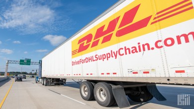 A gold-and-white DHL Supply Chain tractor trailer seen from the side rolls down the highway.