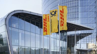 Gold-and-red DHL flags flying in front of glass headquarters building.