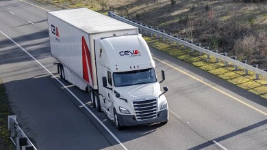 A white truck with Ceva Logistics logo heads down the highway, approaching the camera on an overpass.