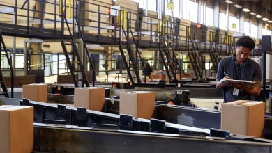 A UPS warehouse worker checks packages on a conveyor belt.