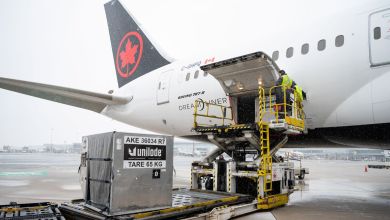 A large cargo container is loaded into an Air Canada 787 Dreamliner on a rainy day.