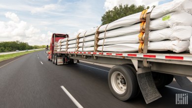 A red tractor pulling covered items on a flatbed trailer on a highway