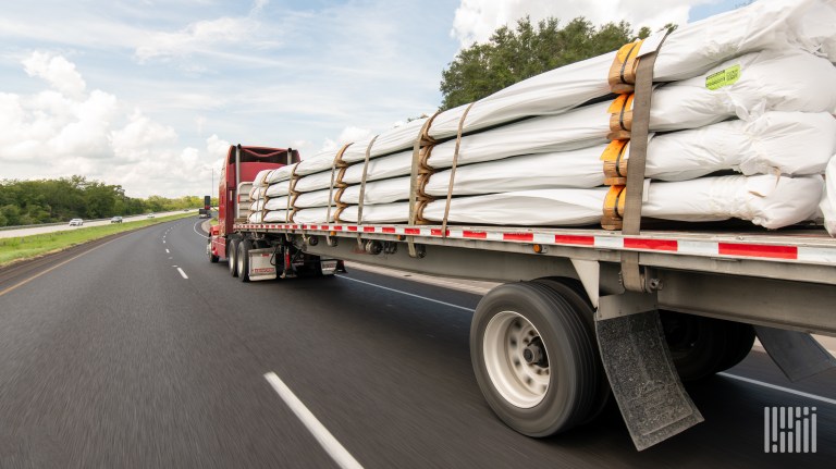 A red tractor pulling covered items on a flatbed trailer on a highway