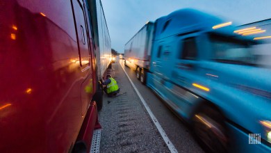 Truck driver repairing truck as traffic speeds by.