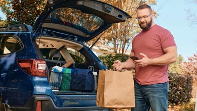 An independent package driver loads bags of goods into the tailgate of his car.
