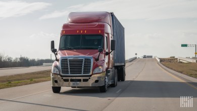 a maroon tractor pulling a blue ocean container on a highway