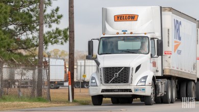 A Yellow daycab pulling two trailers near a terminal