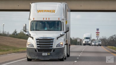 a closeup of a white Werner tractor pulling a trailer near an underpass on a highway
