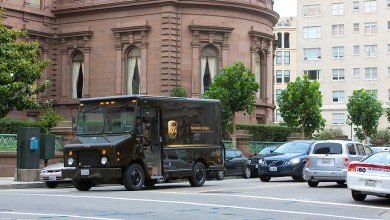 A brown UPS delivery van cruises a city street.