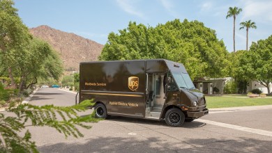 A brown UPS delivery van moves through neighborhood streets of Palm Springs, California, with palm trees in the background. Van is making a turn.