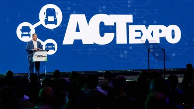 Erik Neandross, producer of ACT Expo and president of TRC’s Clean Transportation Solutions, speaks from the main stage podium at ACT Expo. A large blue backdrop displays the ACT Expo logo with connected truck graphics as an audience listens