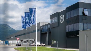 Blue facade of a Kuehen +Nagel warehouse, with blue flags on poles at the entrance.