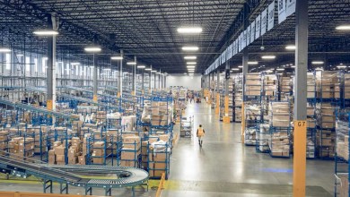 Maersk e-commerce fulfillment warehouse interior with conveyor belts, tall blue shelving packed with parcels, and a worker walking the aisle