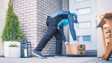 An Amazon delivery driver in two-tone blue uniform places a package at a residential doorstep.