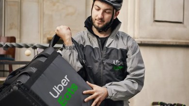 Close up of an Uber Eats courier with a soft cooler and Uber Eats jacket, wearing a bike helmet.