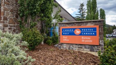 A stone-sided Canada Post office with red sign next to it.