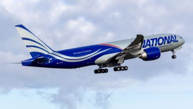 A blue-themed National Airlines 777 jet takes off into the sky, as seen from the side rear.