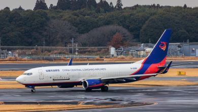 A blue-tailed China Central Longhao Airlines Boeing 737-800 freighter seen on an airport taxiway with trees in the background.