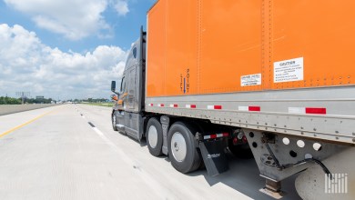 closeup of a gray Schneider tractor pulling an orange trailer on a highway