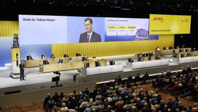 Large TV screens and audience in an auditorium for a DHL annual meeting.
