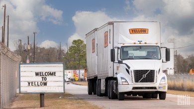 A Yellow daycab leaving a terminal with two pup trailers