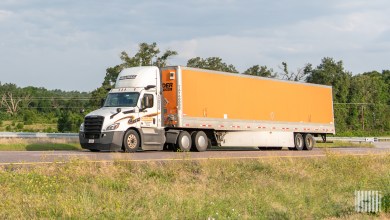 a white Schneider daycab pulling an orange Schneider dryvan trailer
