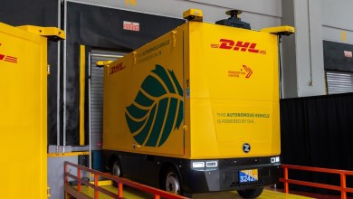 Yellow DHL autonomous vehicle with green leaf logo inside Singapore logistics facility. The driverless electric shuttle displays "This autonomous vehicle is powered by DHL" and is used for hub-to-hub transfers at the Advanced Regional Center.