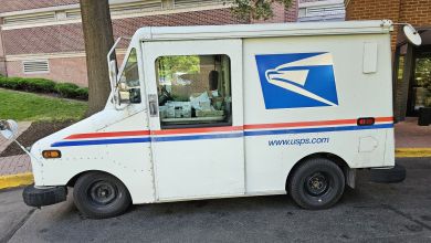 A side view of a U.S. Postal Service delivery van in front of an apartment building.