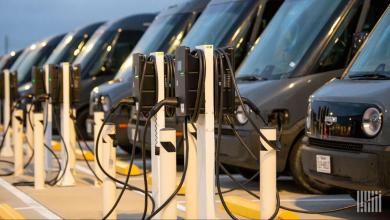 A row of electric vehicle chargers in front of a group of electric delivery vans