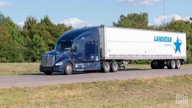 a dark blue sleeper cab pulling a Landstar trailer on a sideroad