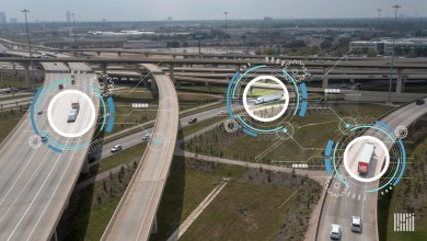 Aerial view of trucks navigating a multi-level highway interchange with digital overlays of targeting circles, gears and circuit patterns representing AI-powered freight tracking and logistics automation